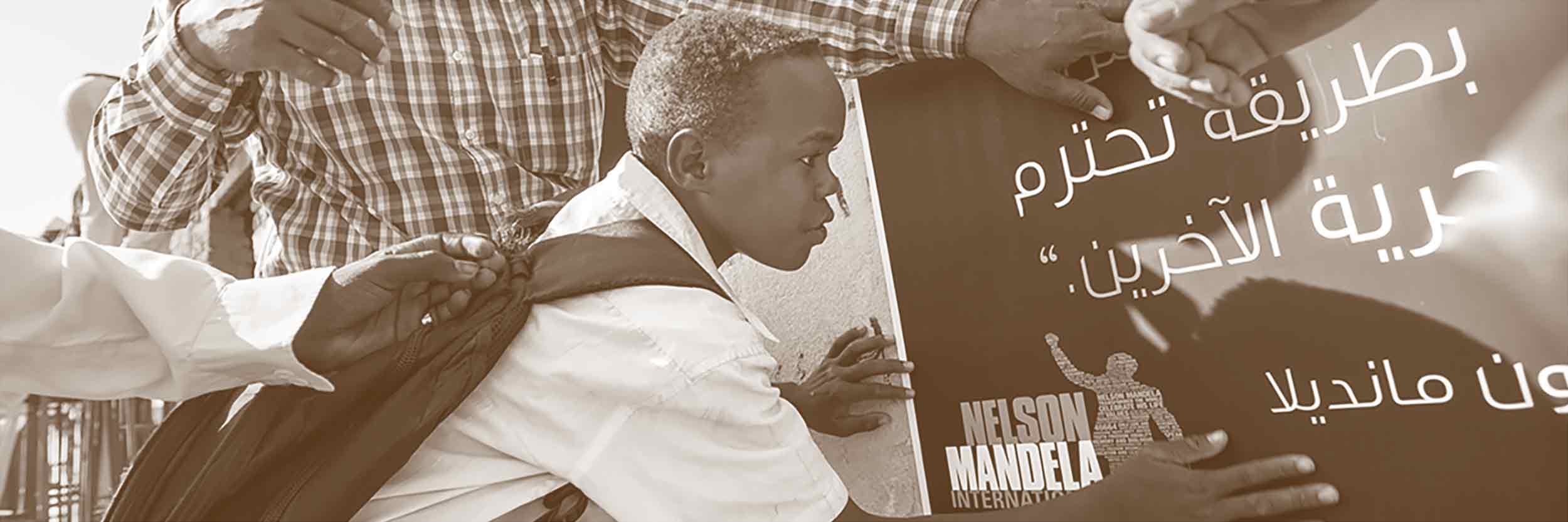 Des soldats de la paix de la Mission des Nations Unies au Darfour mettent place avec des étudiants une affiche pour la commération de la Journée Nelson Mandela dans une école primaire du camp d'Al Salaam pour réfugiés près d'El Fasher, Darfour Nord. Copytight ONU / Albert González Farran
