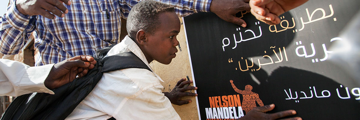 Des soldats de la paix de la Mission des Nations Unies au Darfour mettent place avec des étudiants une affiche pour la commération de la Journée Nelson Mandela dans une école primaire du camp d'Al Salaam pour réfugiés près d'El Fasher, Darfour Nord. Copytight ONU / Albert González Farran