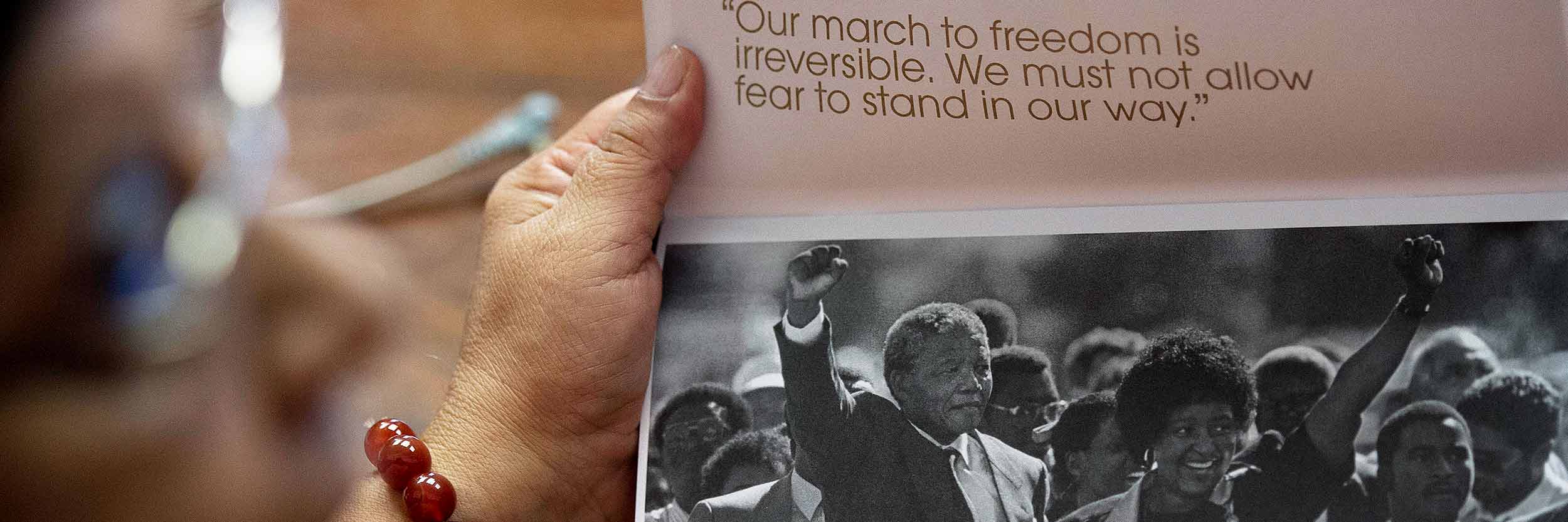 Une femme tient un livret avec une photo de Nelson Mandela levant son poing au côté de sa femme lors d'une mobilisation collective.
