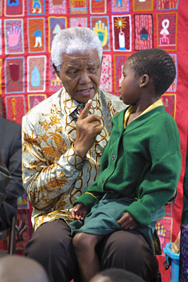 Mr. Mandela with a child on his lap, talking to her. Taken during meetings about HIV/AIDS in November 2004.