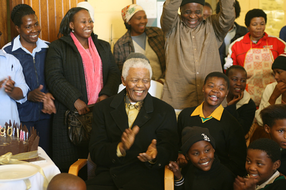 Mr. Mandela, surrounded by children, clapping his hands & 90th birthday cake on the table
