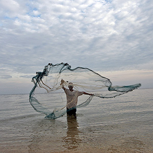El pescador en Timor Leste lanza su red en el agua para atrapar peces pequeños. Foto ONU/Martine Perret