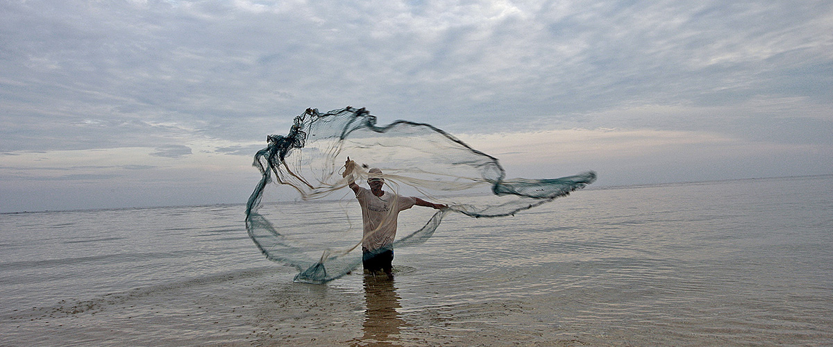 El pescador en Timor Leste lanza su red en el agua para atrapar peces pequeños. Foto ONU/Martine Perret