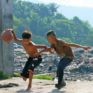 Rex (izquierda), de 14 años, juega al baloncesto con su amigo con un basurero de fondo. Lleva dos años viviendo ahí con su familia.
