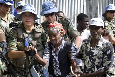 Soldados del contingente argentino de  la Misión de Estabilización de las Naciones Unidas en Haití (MINUSTAH) ayudan a una anciana a caminar hacia un centro de distribución de la ayuda alimentaria donada por el gobierno de México.