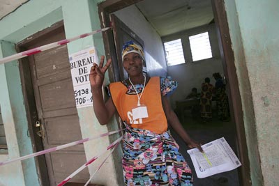 Член Независимой избирательной комиссии дает сигнал зайти в здание избирательного участка следующим двум избирателям для участия в выборах в Демократической Республике Конго.