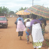 Women walking with children on their backs while a car passes by.