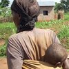 A woman walks with a baby on her back.